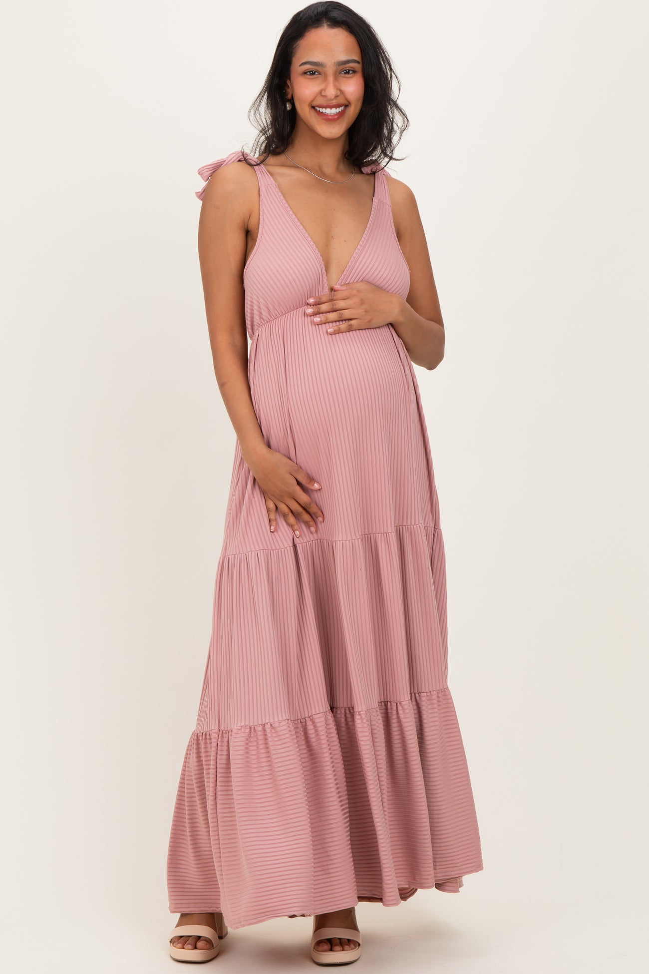 woman wearing a pink striped maternity maxi dress with tie straps and holding her baby bump
