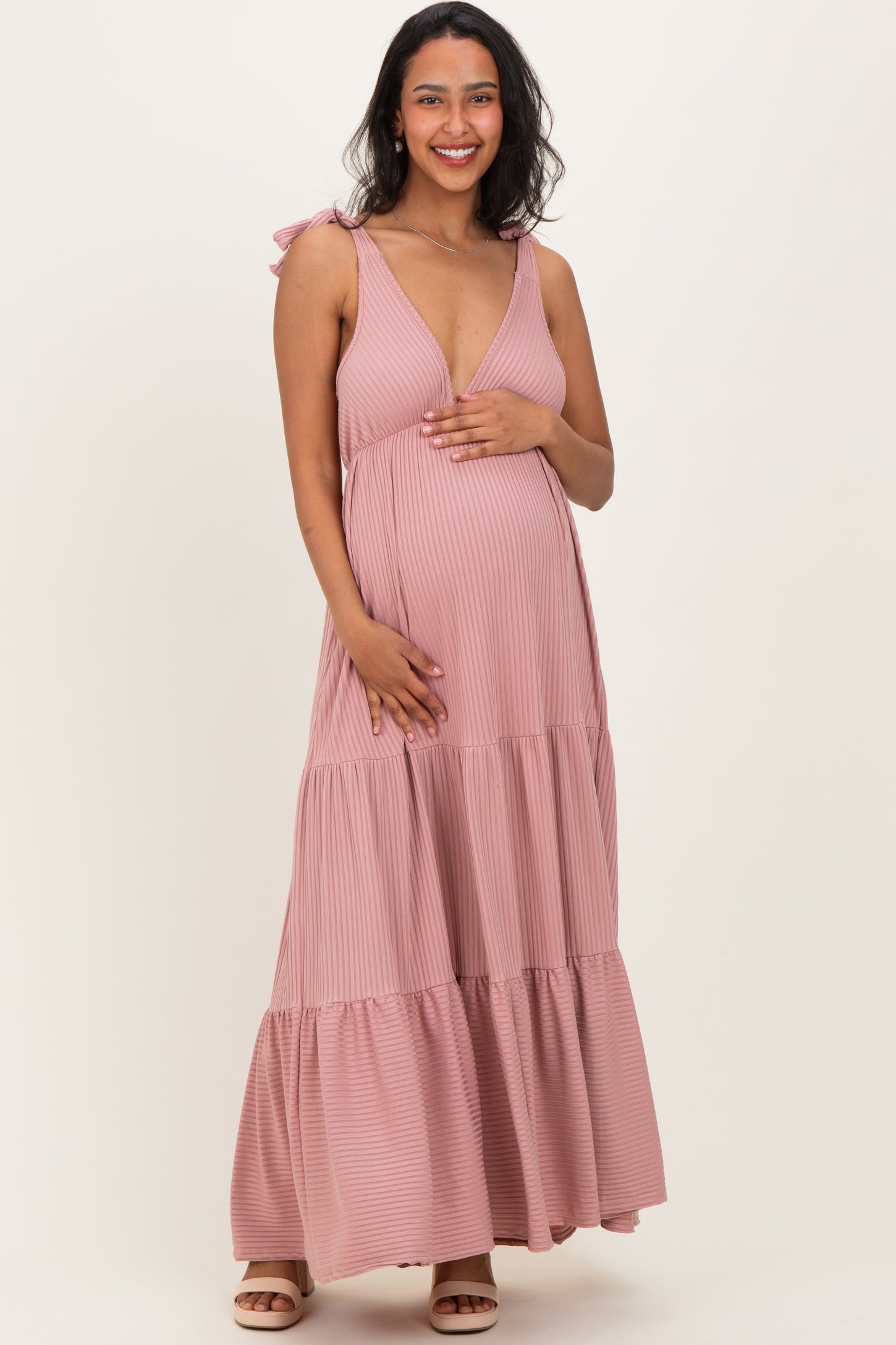 woman wearing a pink striped maternity maxi dress with tie straps and holding her baby bump
