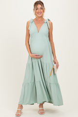 woman wearing a mint green maternity maxi dress with tie straps and a baby bump, holding a clutch purse