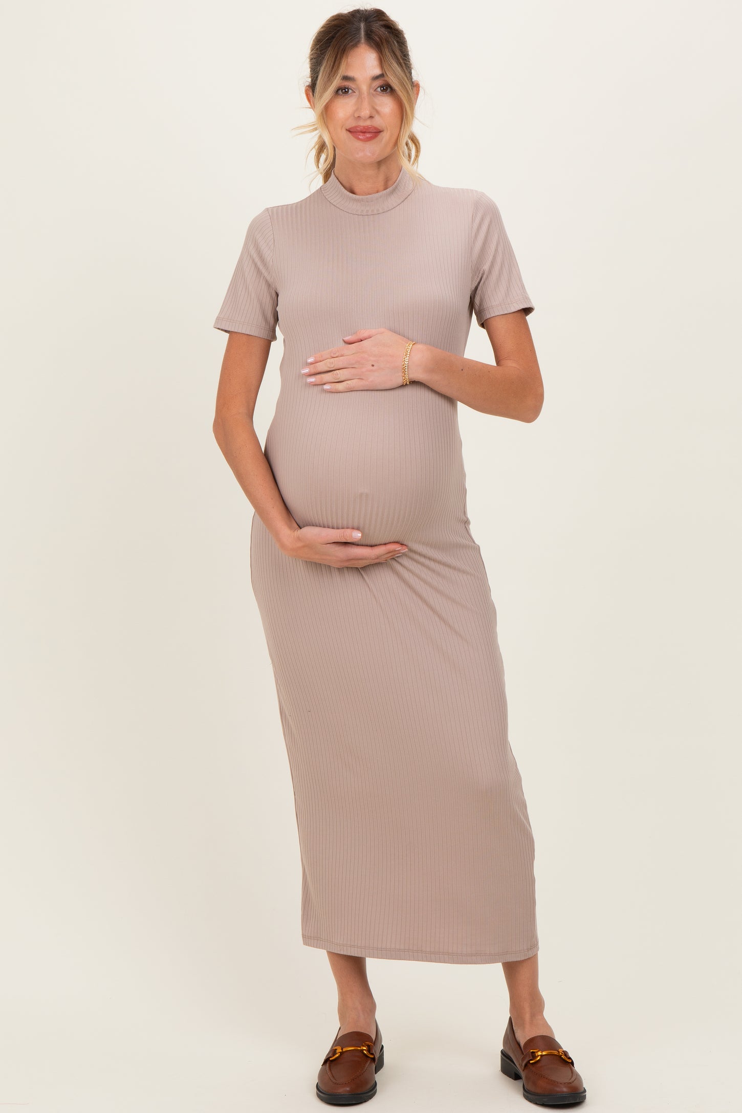 woman wearing a taupe ribbed maternity maxi dress and gently cradling her baby bump