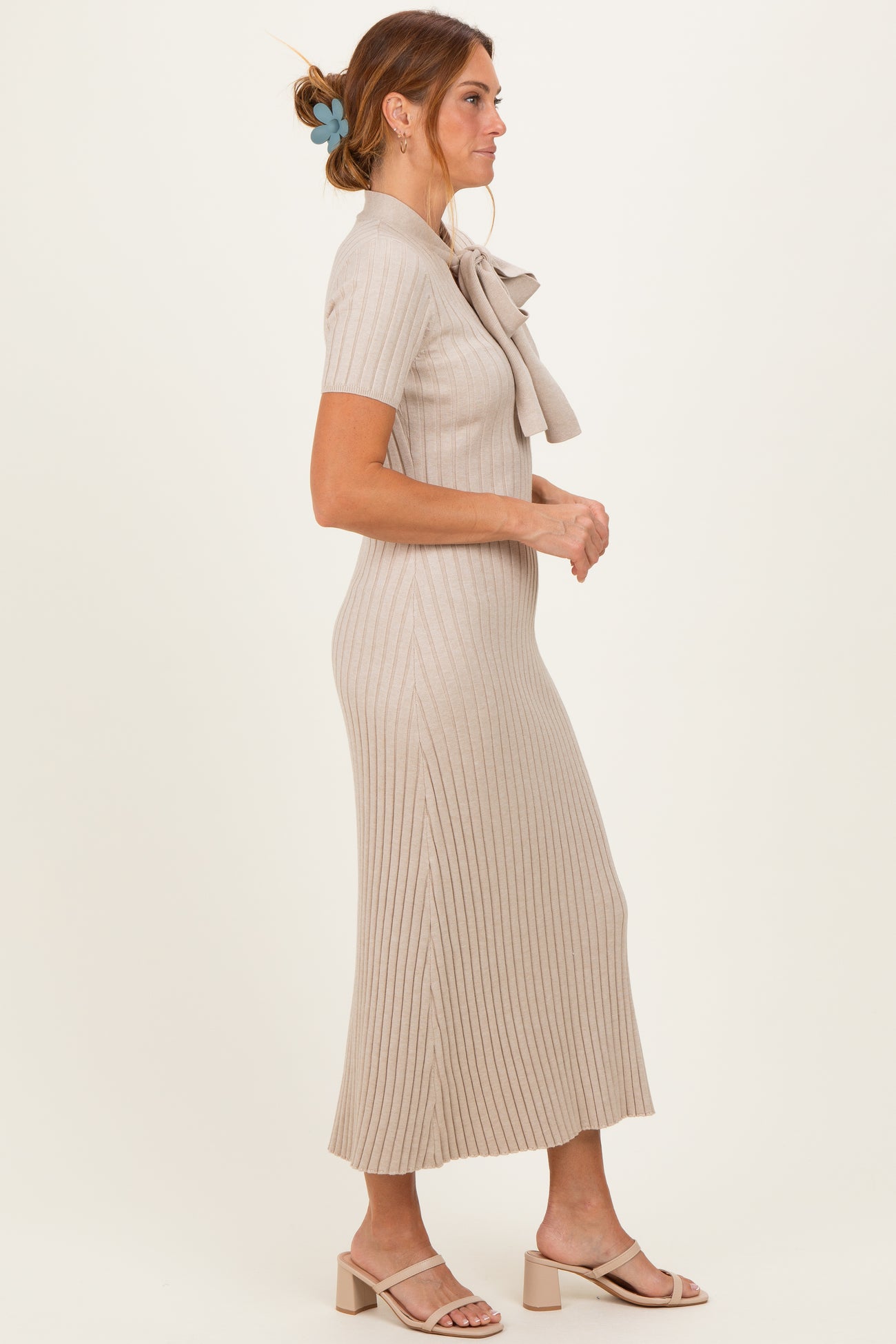 woman wearing a beige ribbed midi dress with a bow collar and short sleeves, standing in profile