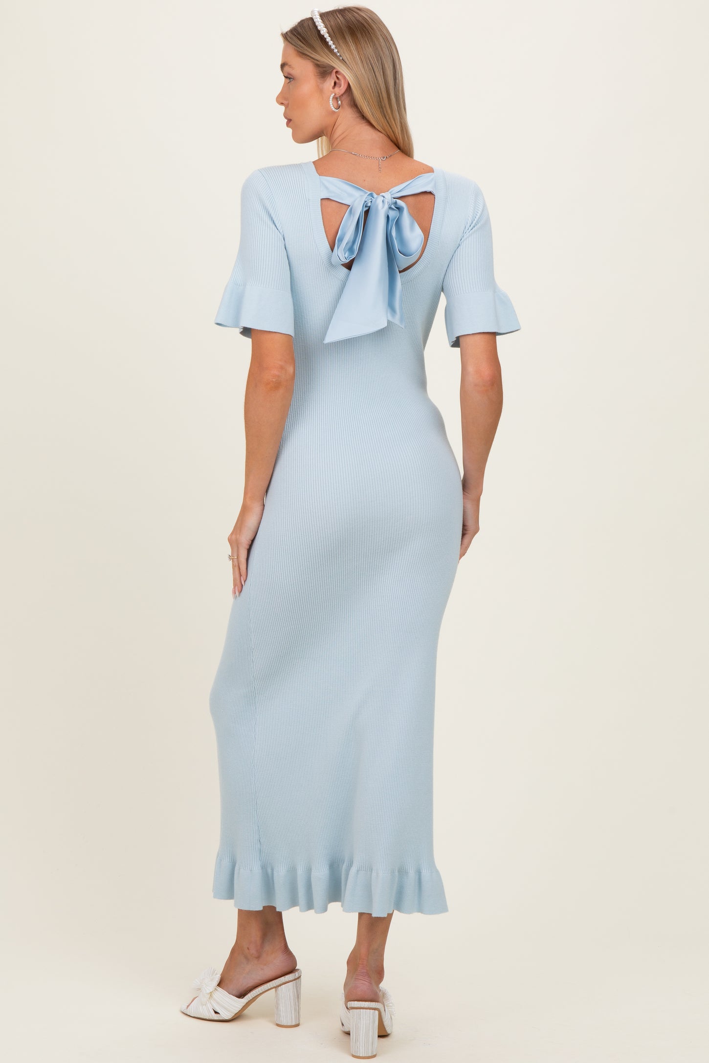 woman wearing a light blue ribbed maternity dress with a bow detail at the back and flared sleeves