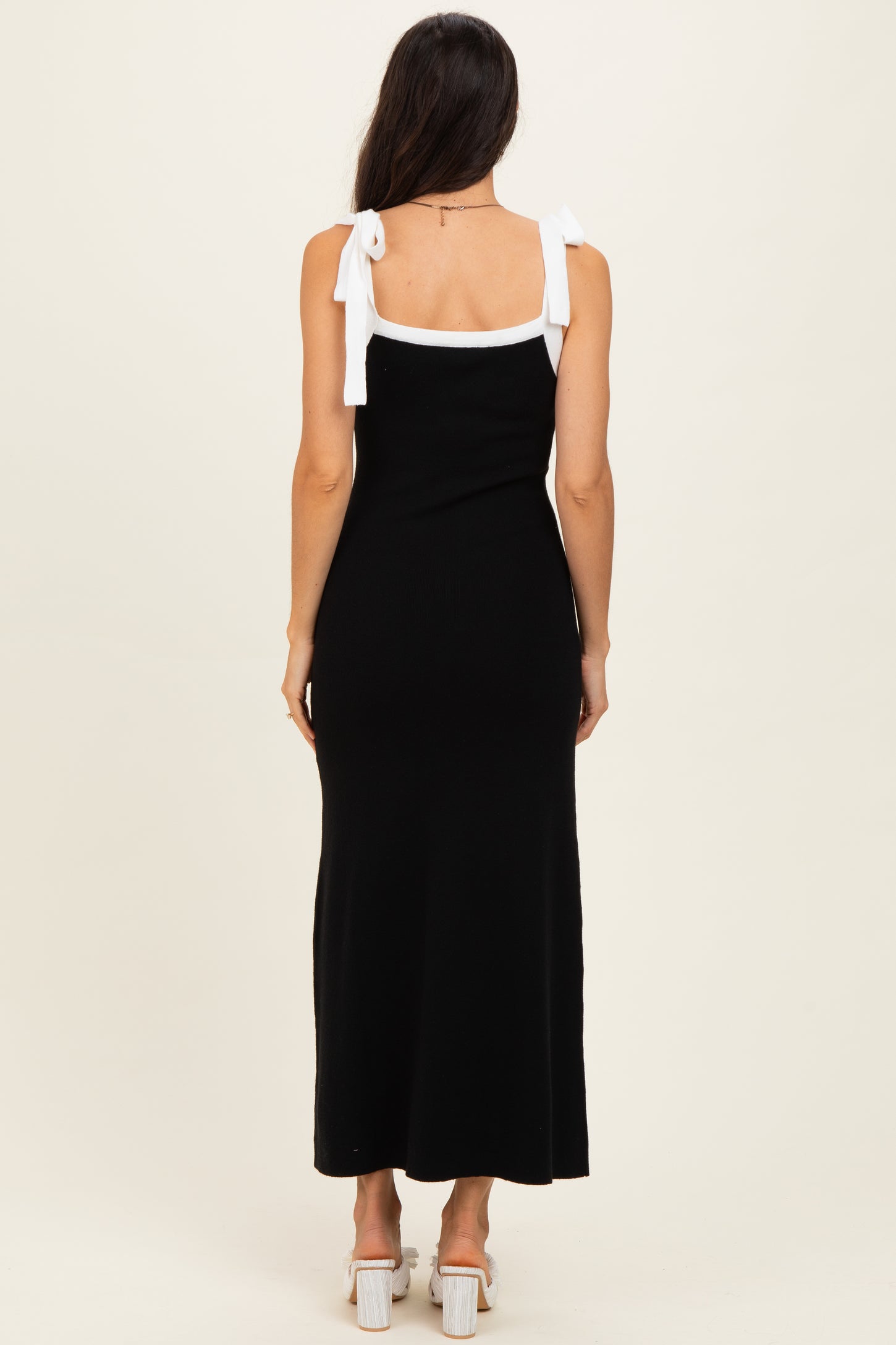 woman wearing a black maxi dress with white tie shoulder straps, seen from the back