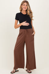 woman wearing a black short sleeve top and brown striped maternity wide-leg pants, holding her baby bump
