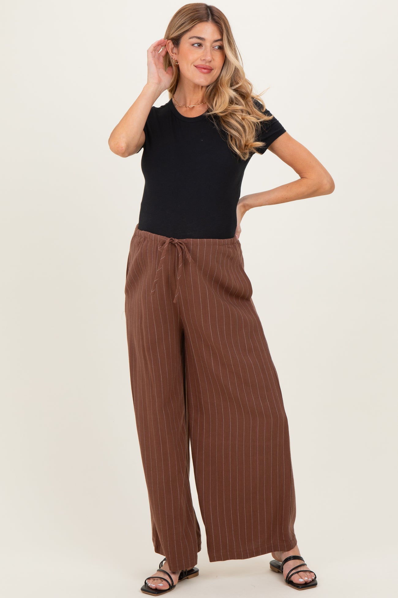 woman wearing a black short sleeve maternity top and brown striped wide leg maternity pants