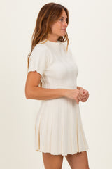 woman wearing a cream short sleeve ribbed mini dress with a pleated skirt detail