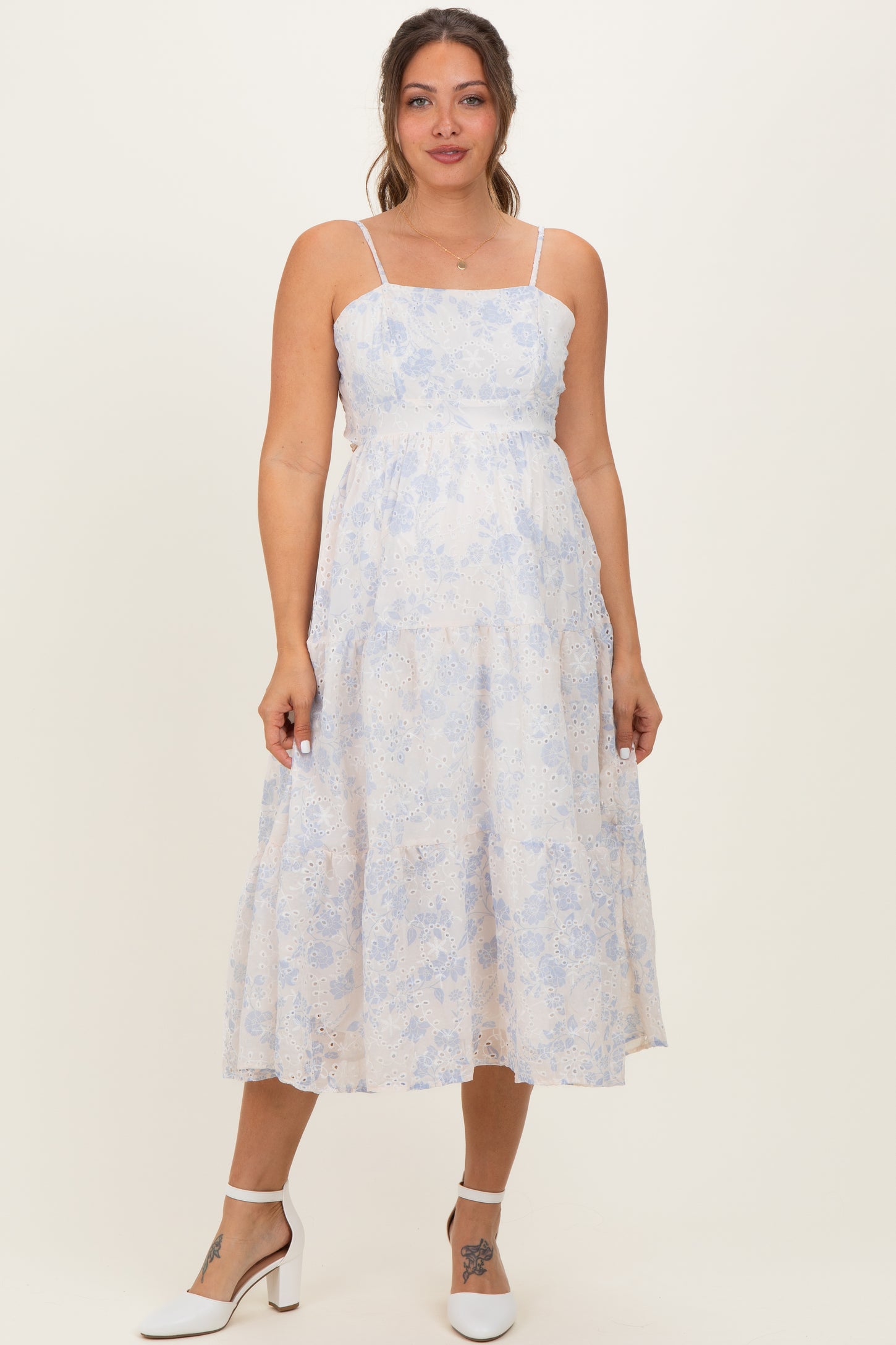woman wearing a light blue floral maternity dress with spaghetti straps and a tiered skirt, showing her baby bump