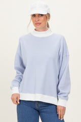 woman wearing a light blue striped oversized sweatshirt with a white collar and cuffs, paired with a white cap