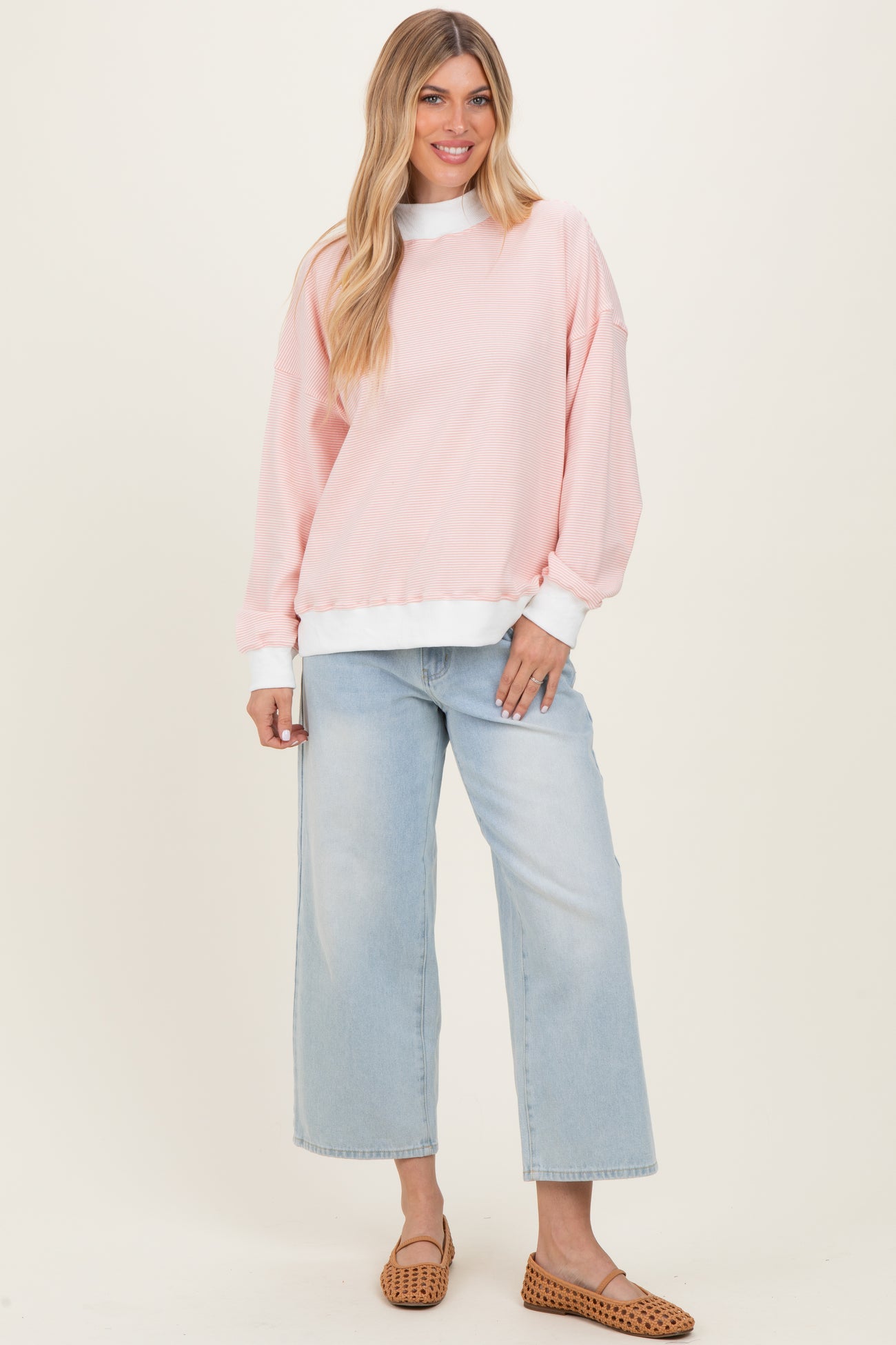 woman wearing a pink oversized sweatshirt with white accents and light blue wide-leg jeans