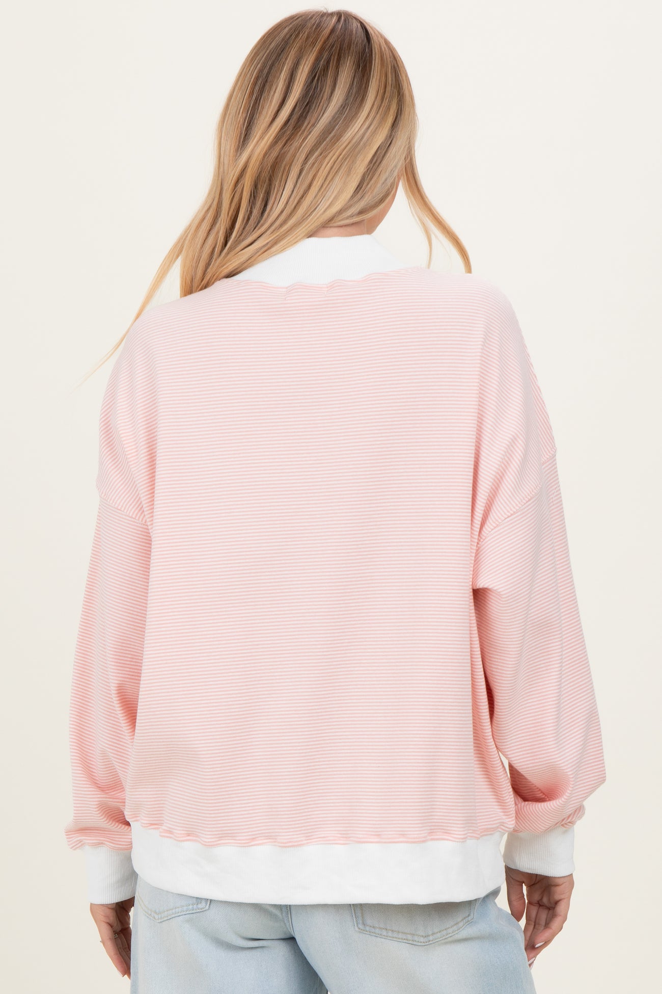 woman wearing a light pink striped oversized sweatshirt with white cuffs and hem, shown from the back