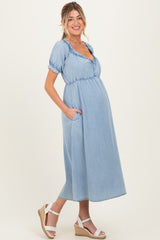 woman wearing a light blue denim maternity dress with short puff sleeves and pockets, showing her baby bump