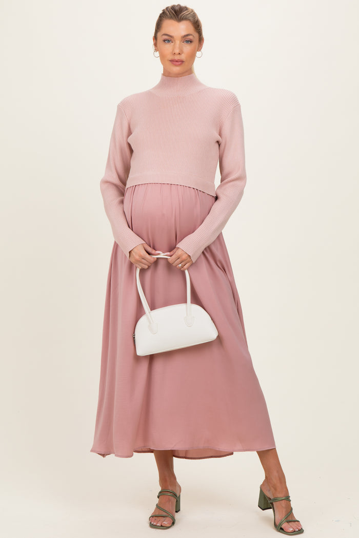 woman wearing a light pink ribbed maternity sweater and a flowy mauve maxi skirt, holding a white handbag and showing her baby bump