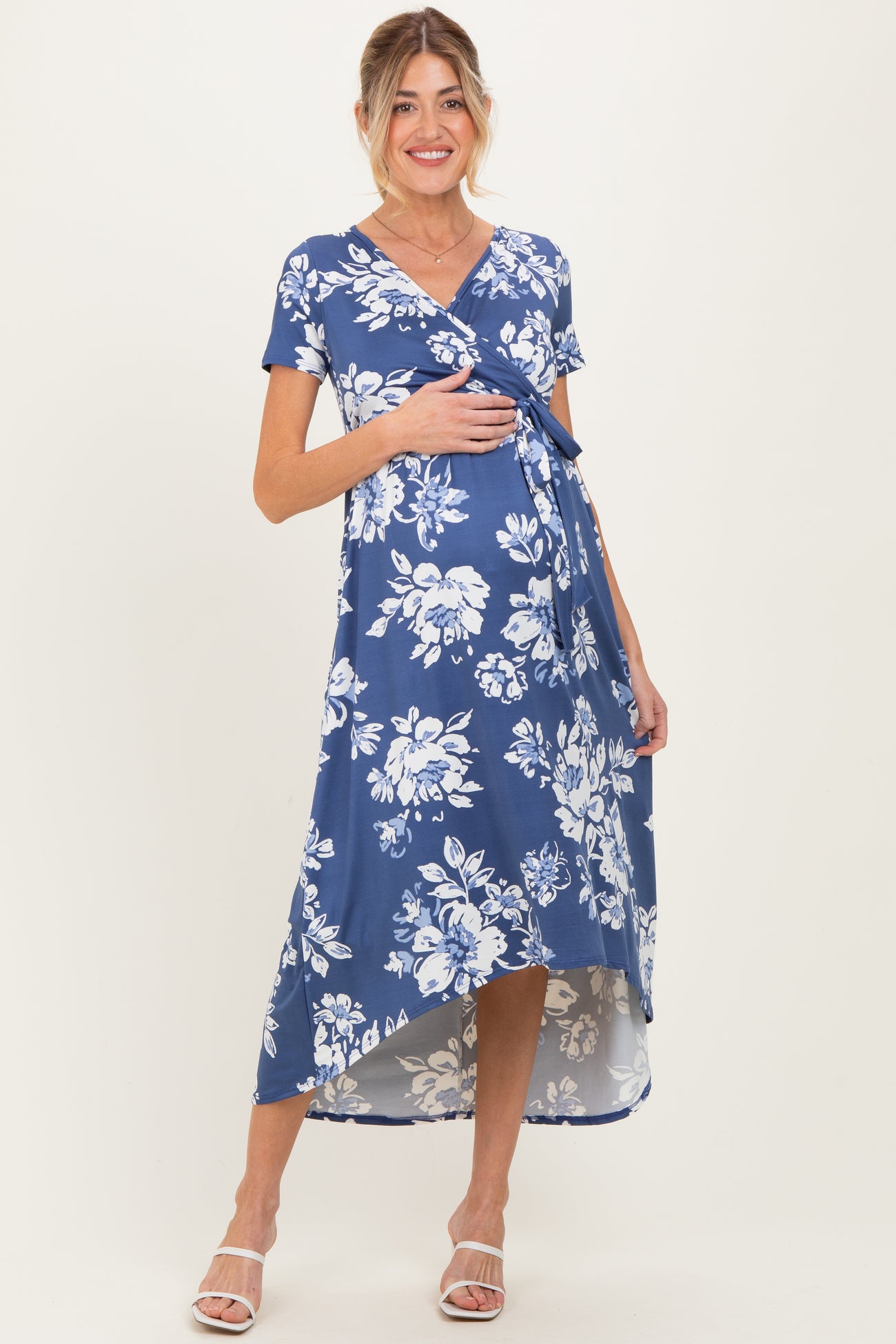 woman wearing a navy blue floral print maternity dress with short sleeves and a tie front, holding her baby bump