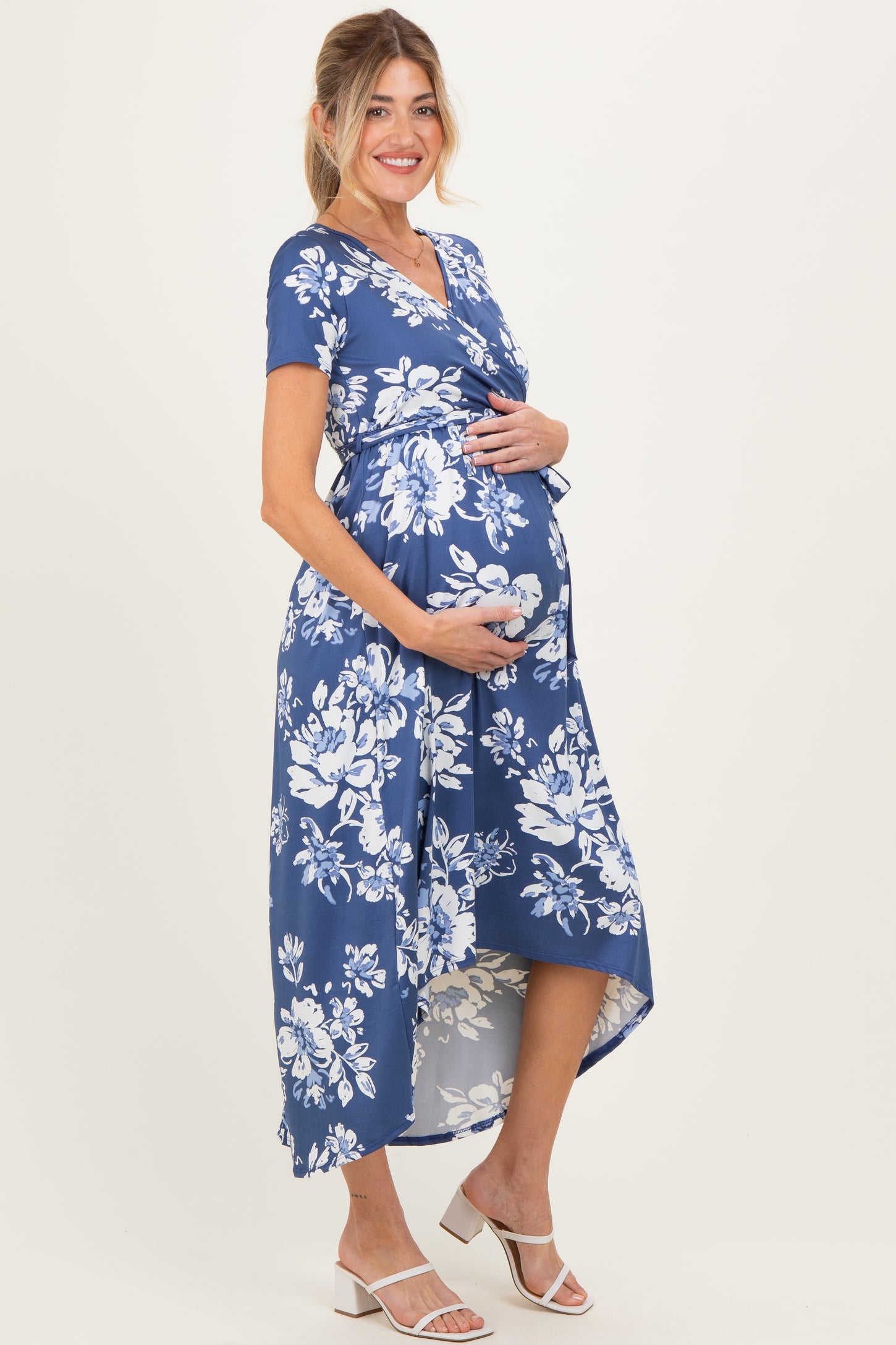 woman wearing a blue floral maternity dress with a high-low hem and holding her baby bump