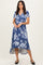 woman wearing a blue floral wrap dress with short sleeves and a high-low hemline, standing and smiling