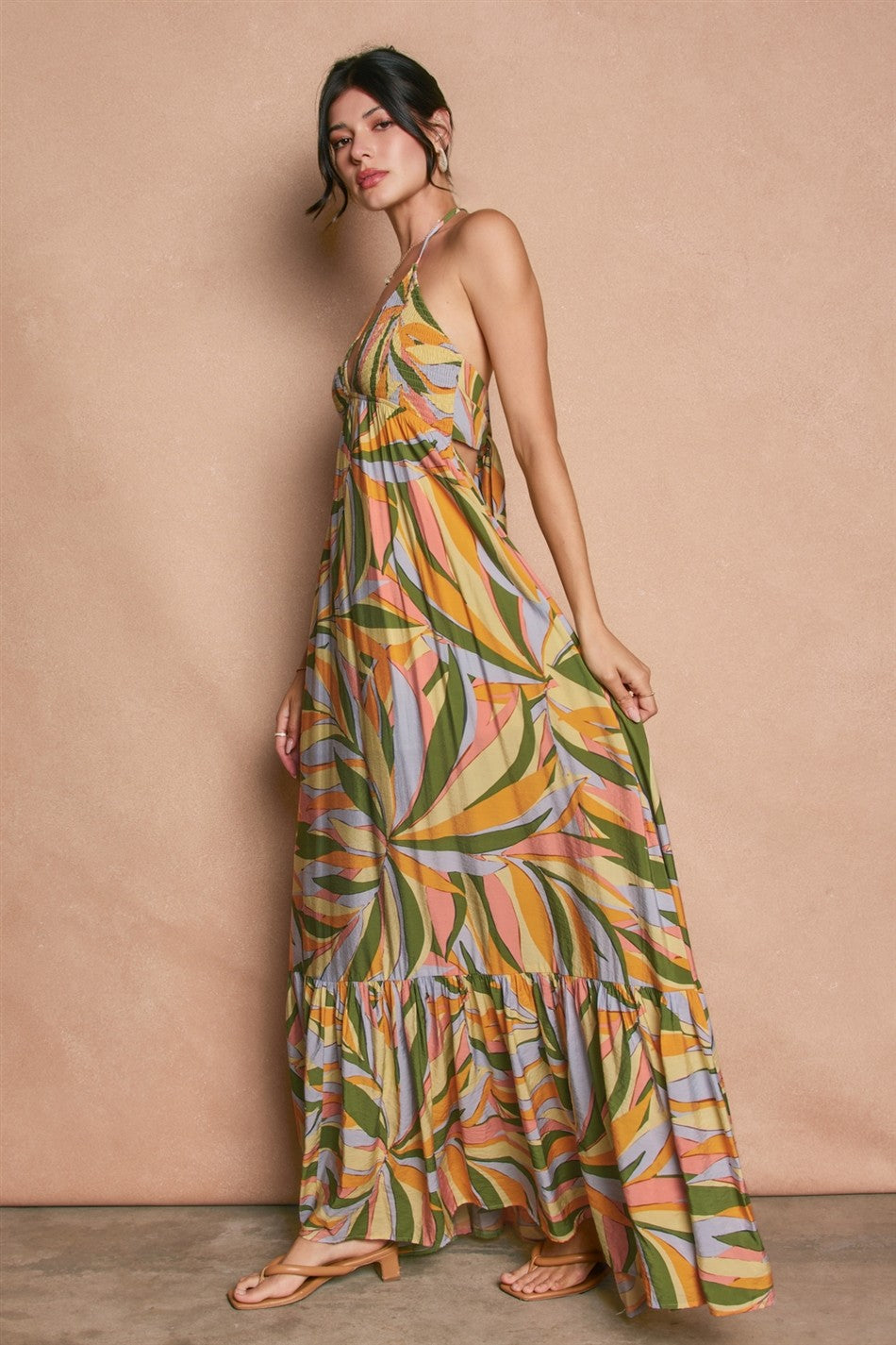 woman wearing a colorful leaf print maxi dress with a tiered skirt and adjustable straps