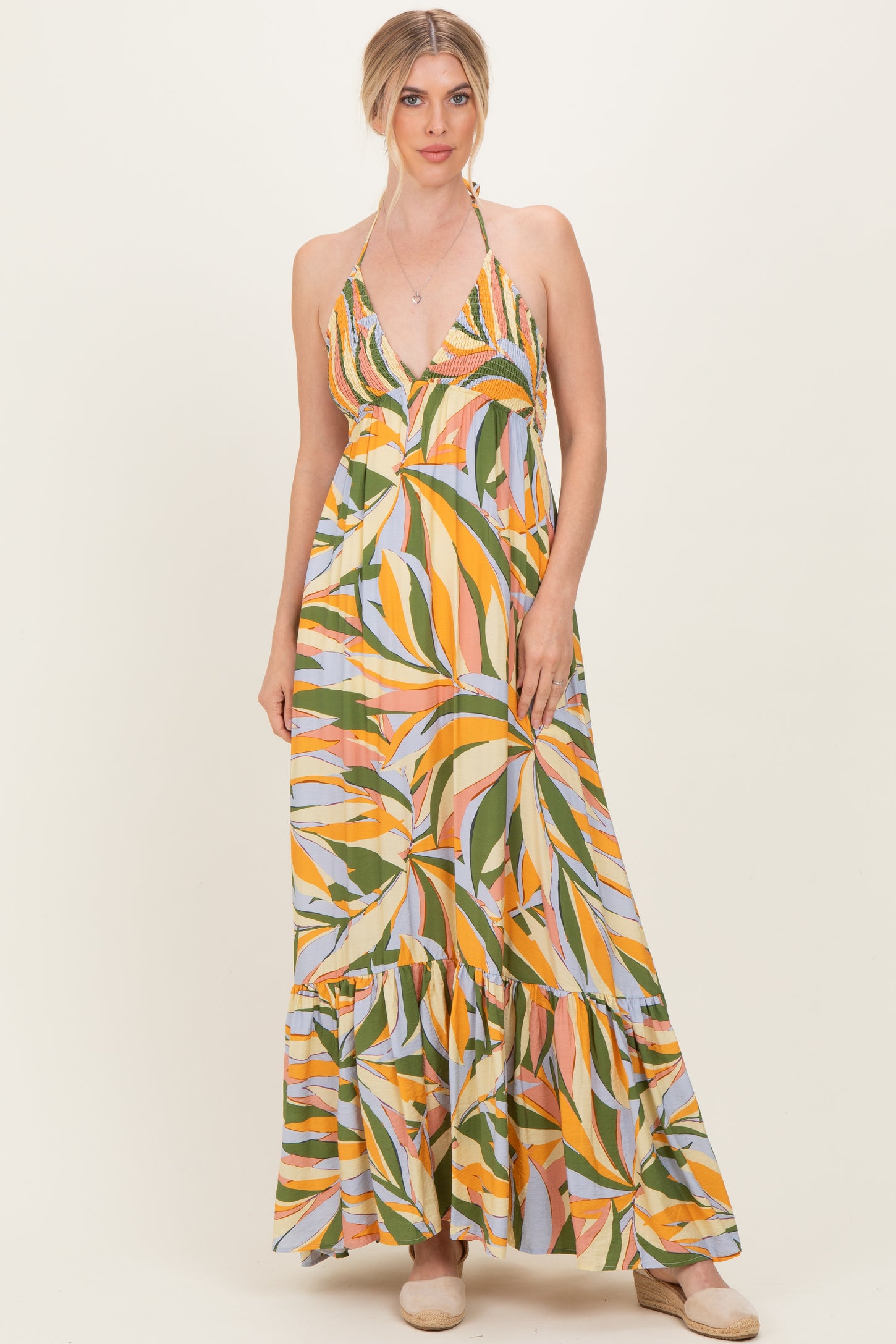 woman wearing a multicolored halter neck maxi dress with a tiered ruffle hem and a vibrant leaf print