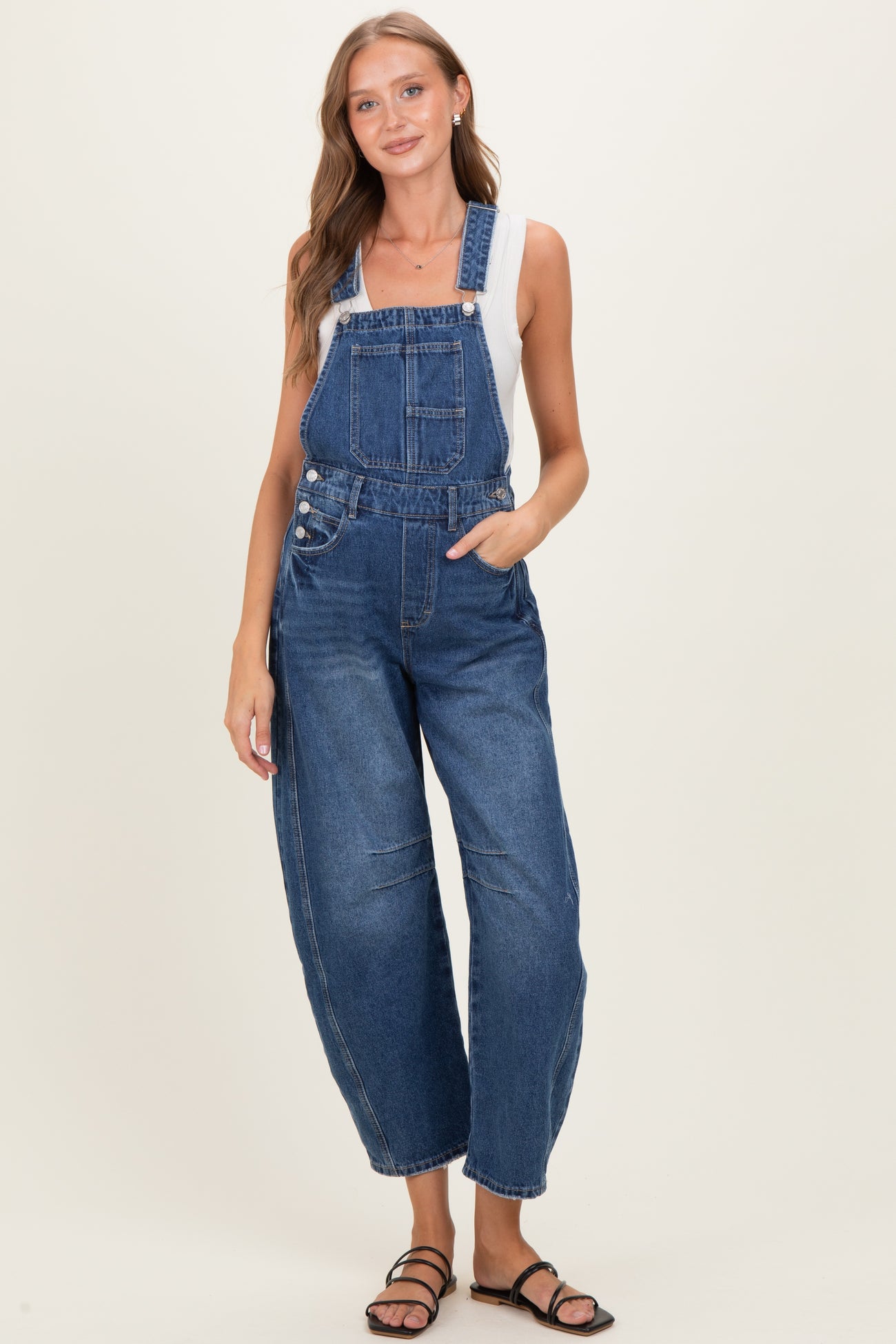 woman wearing a blue denim maternity overall with a fitted bodice and wide legs, styled with a gray tank top