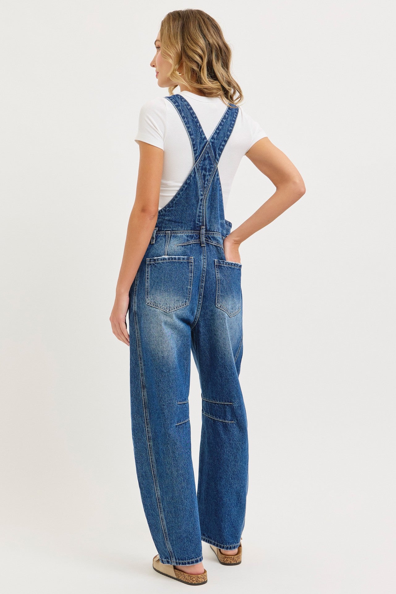 woman wearing a white t-shirt and blue denim overalls, viewed from the back