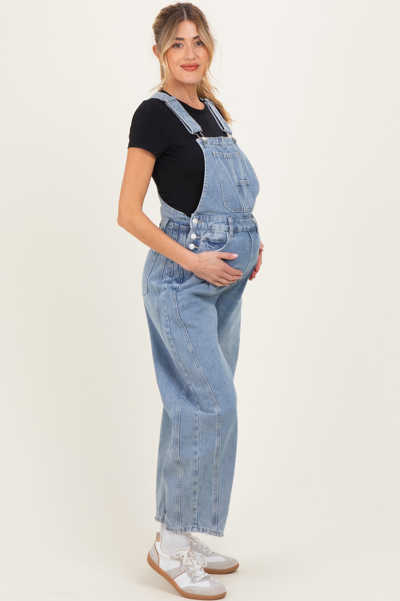 woman wearing a light blue maternity overall and holding her baby bump