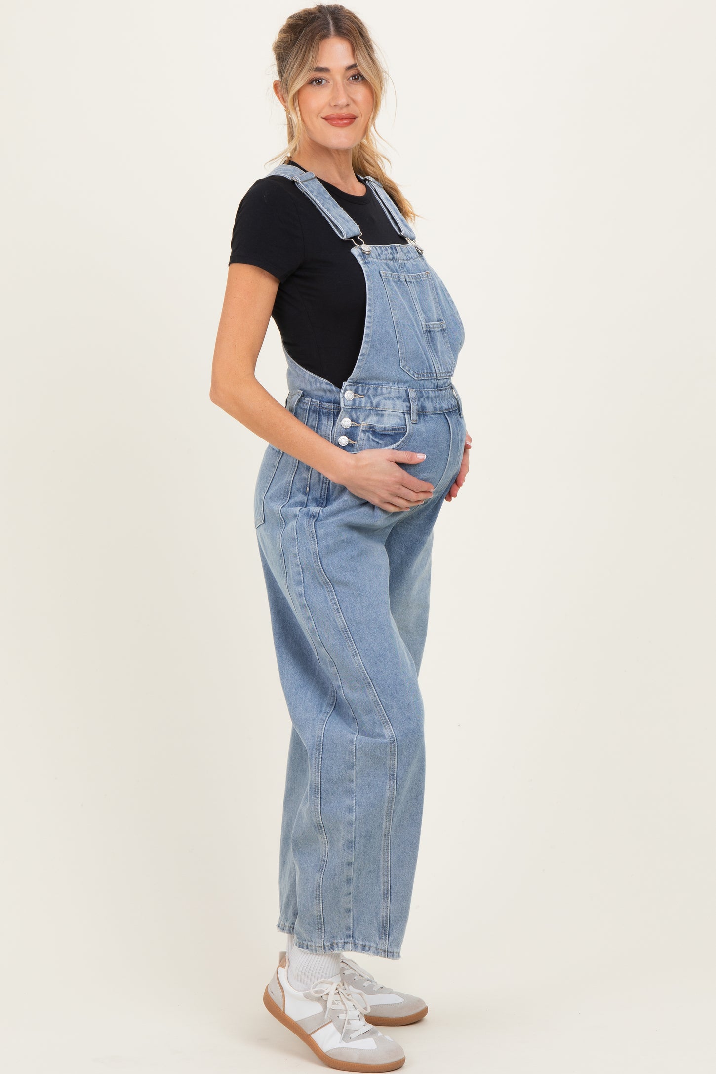 woman wearing a light blue maternity overall and holding her baby bump