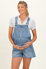 woman wearing a light blue denim maternity overall shorts and holding her baby bump