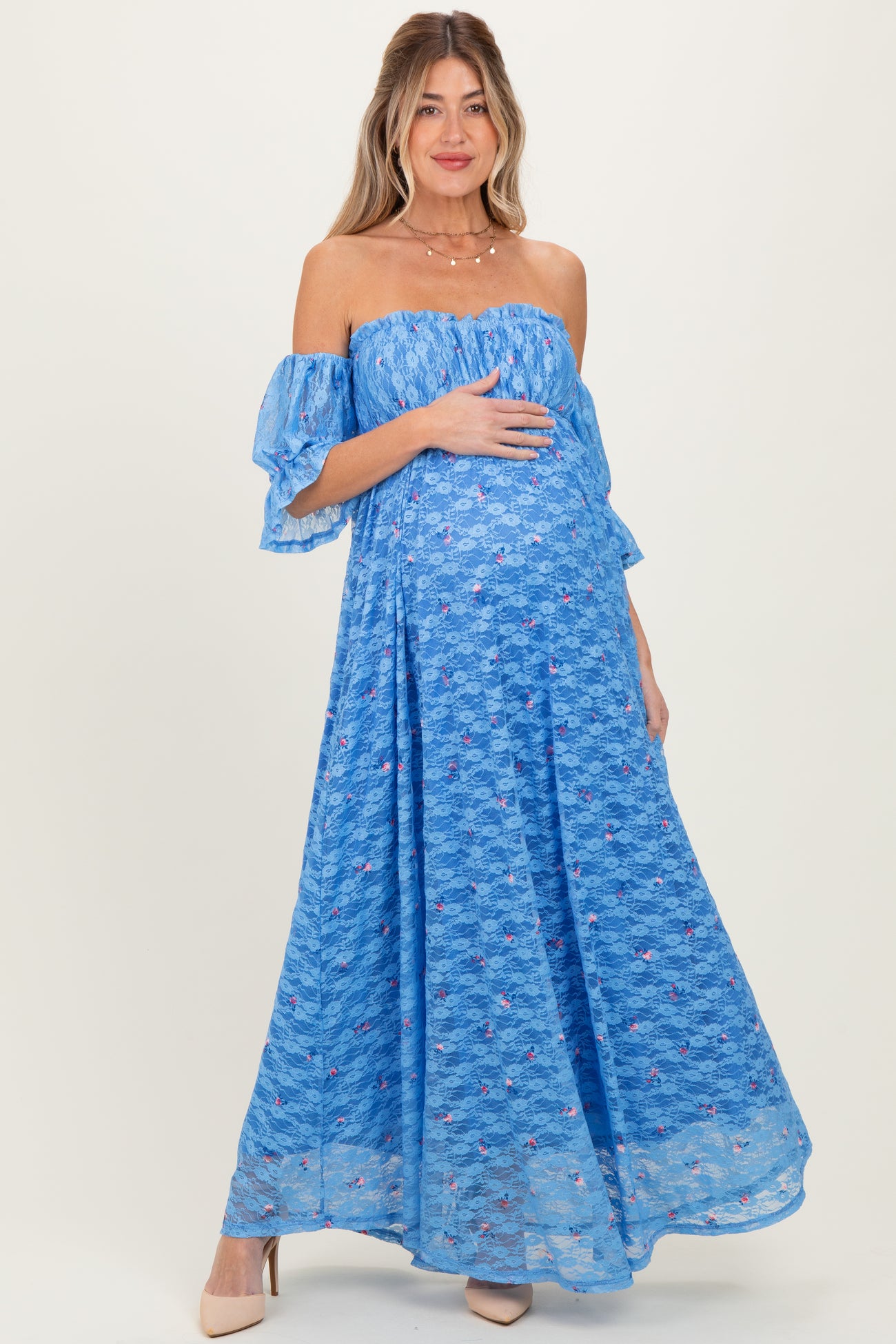 woman wearing a light blue off-the-shoulder maternity dress with floral details and holding her baby bump