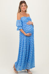 woman wearing a blue off-shoulder maternity maxi dress with floral details and holding her baby bump