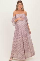 woman wearing a light pink off-the-shoulder maternity gown with flared sleeves and floral details, holding her baby bump