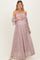 woman wearing a light pink off-the-shoulder maternity gown with flared sleeves and floral details, holding her baby bump