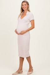 woman wearing a light pink maternity dress with a v-neck and short sleeves, gently holding her baby bump