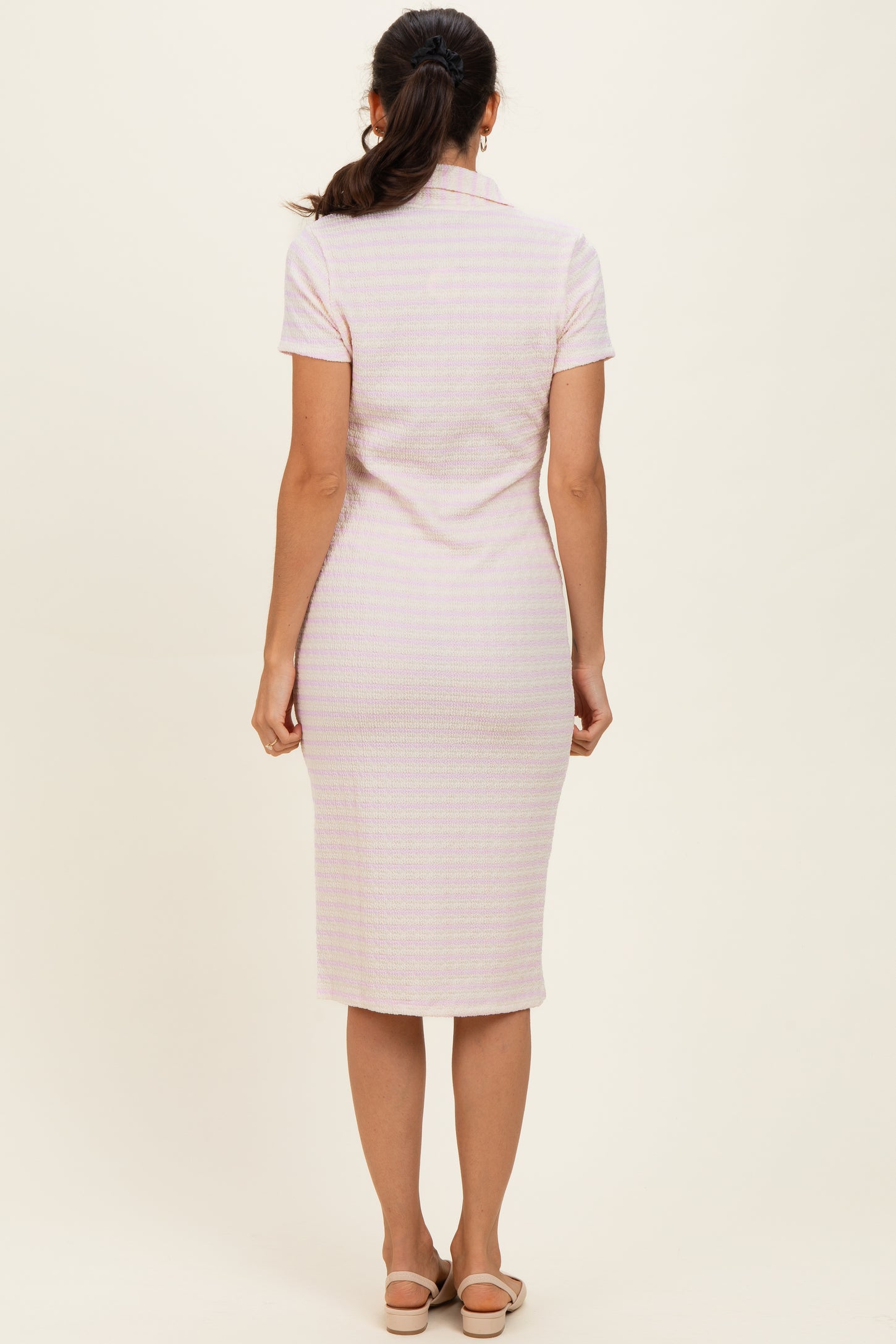 woman wearing a fitted short sleeve pink and white striped midi dress, viewed from the back