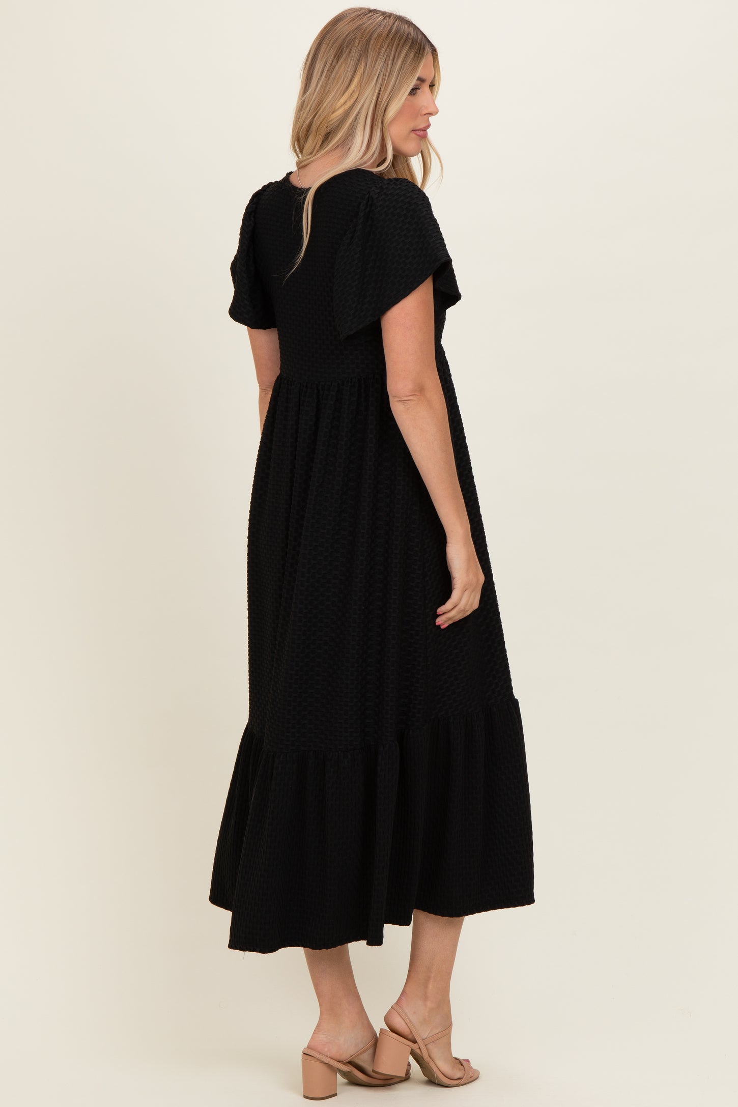 woman wearing a black short sleeve maxi dress with ruffle details, showing the back view and styled with sandals