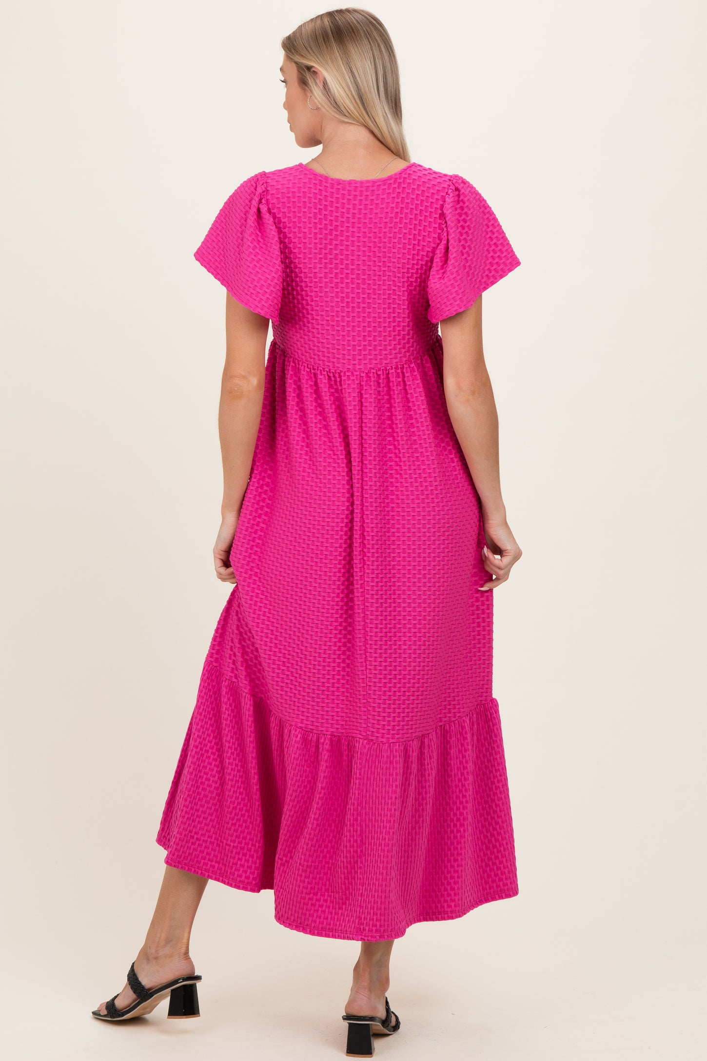 woman wearing a bright pink maternity dress with puff sleeves and a tiered hem, showing the back view