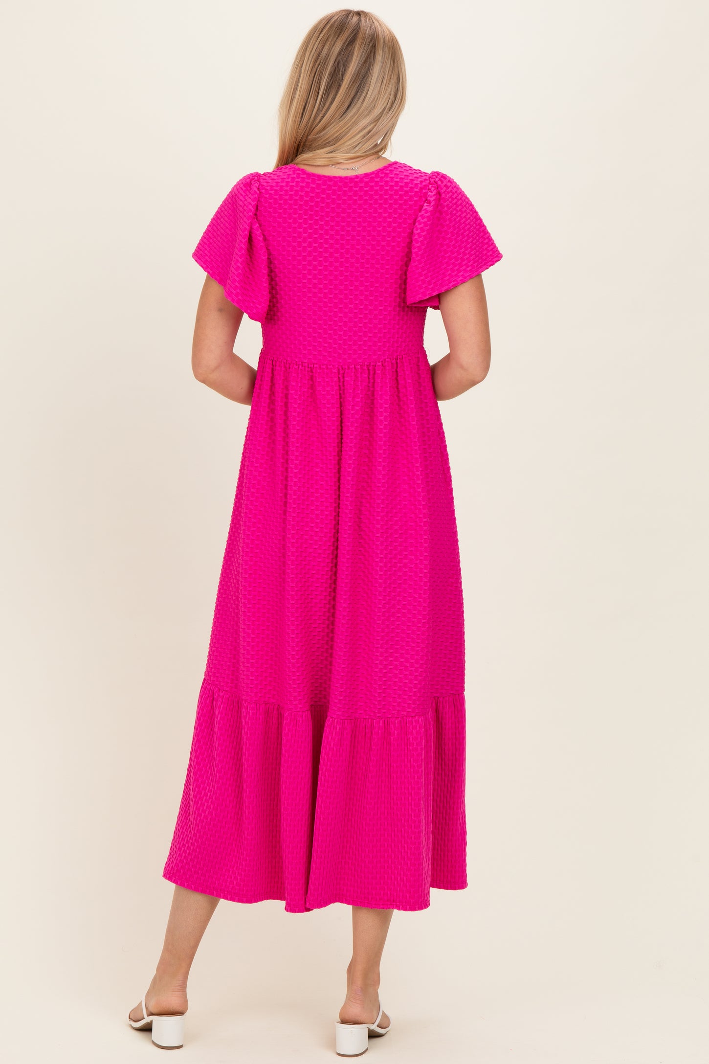 woman wearing a bright pink puff sleeve maxi dress with a tiered skirt, standing with her back to the camera