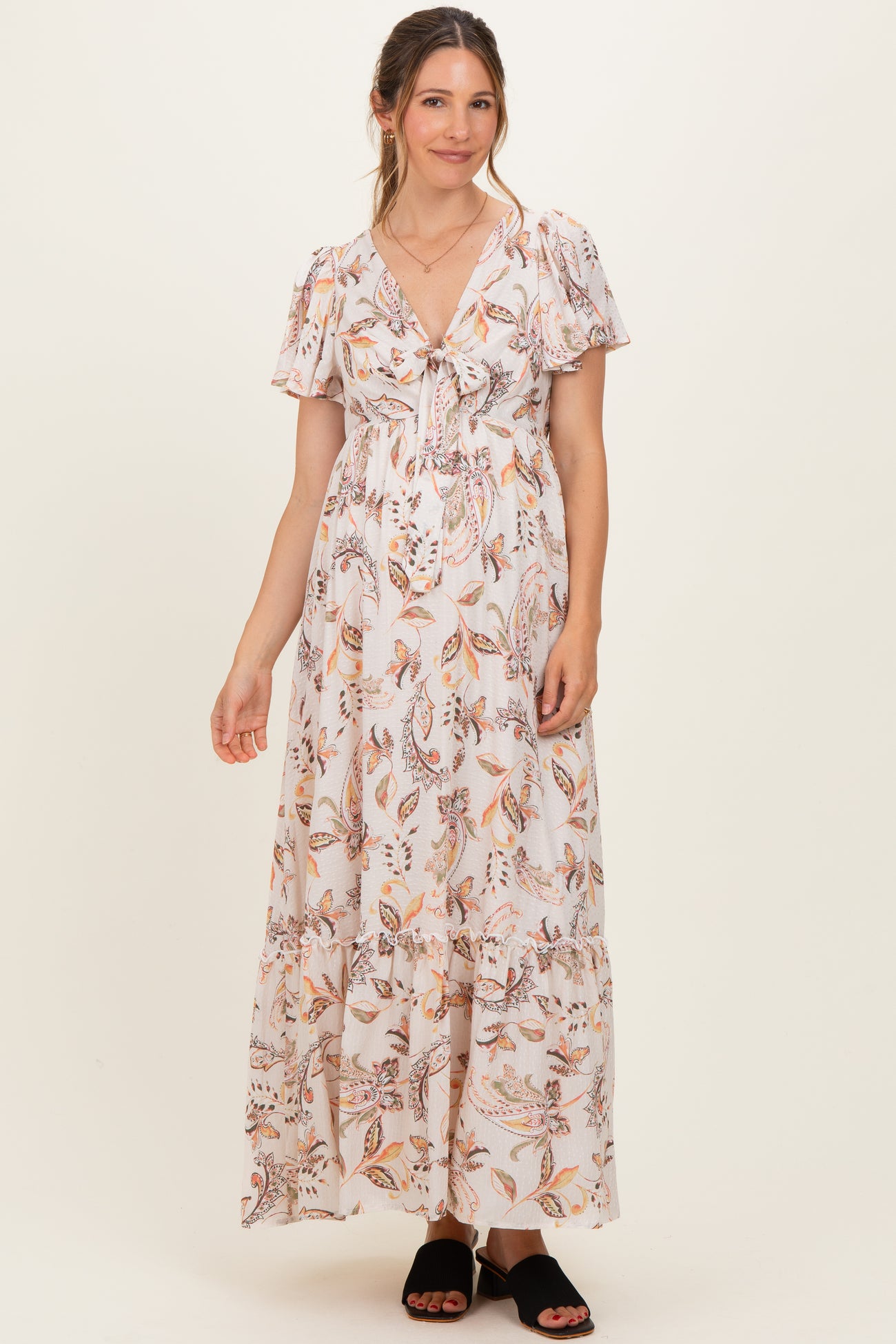 woman wearing a floral printed white maternity maxi dress with short sleeves and a tie front detail, showcasing a baby bump