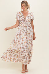 woman wearing a floral print maxi dress with short sleeves and a tie-front detail, standing with one hand raised