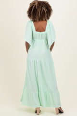 woman wearing a light green maternity maxi dress with flutter sleeves, showing the back view and a flowing silhouette