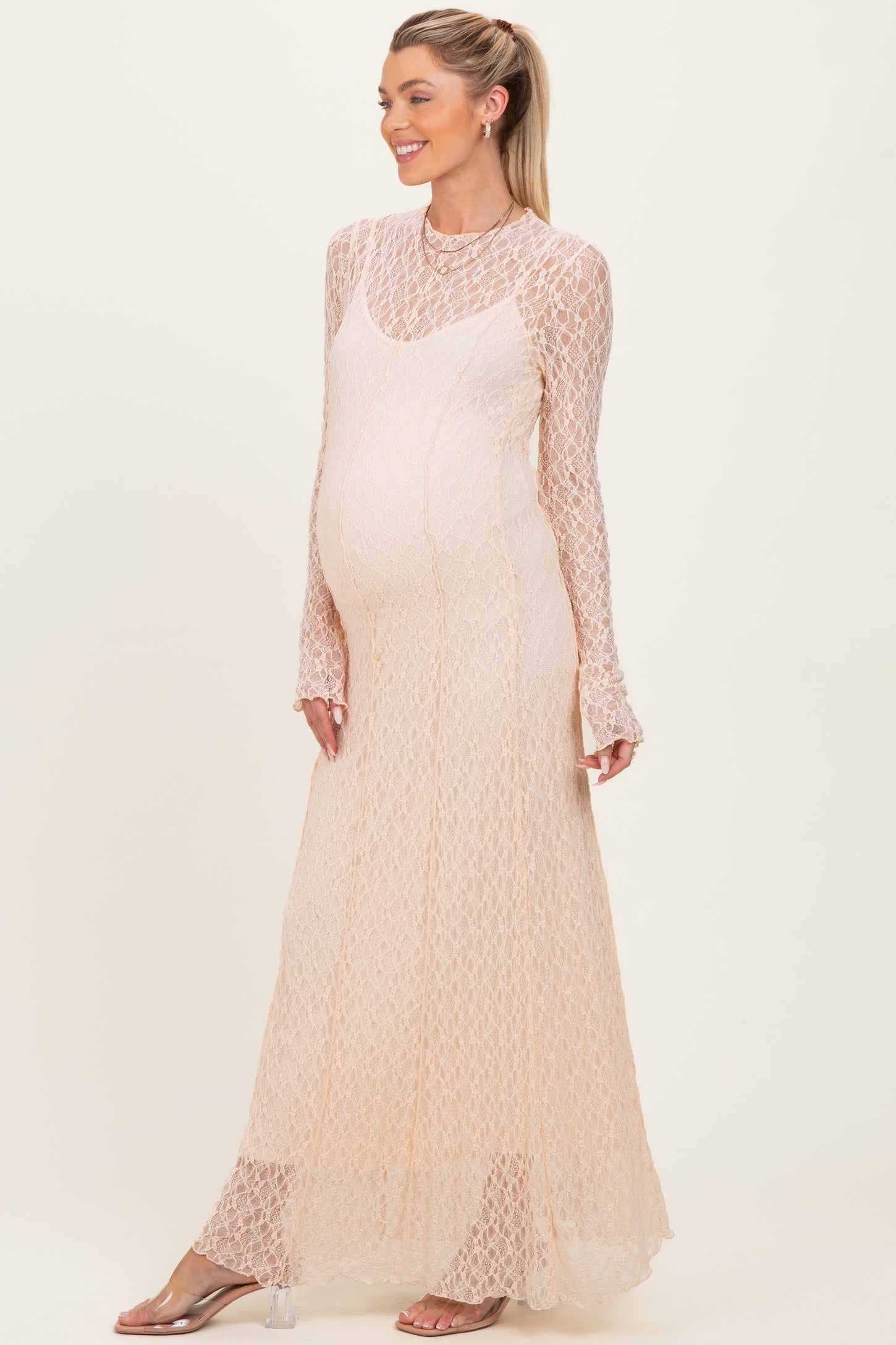 woman wearing a light peach long sleeve maternity dress with a lace design and a visible baby bump