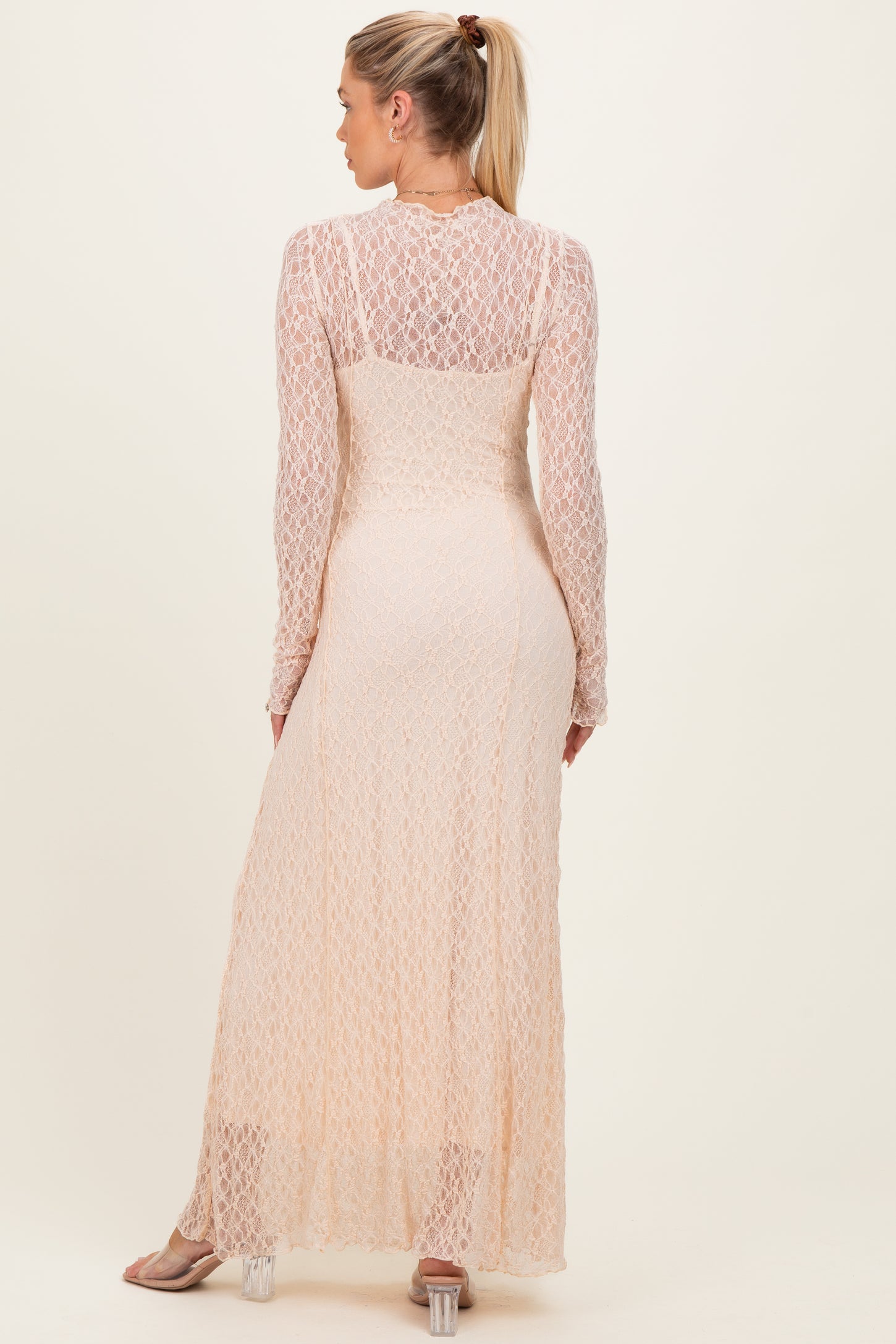 woman wearing a peach long sleeve maternity dress with a lace overlay and a flowing skirt from the back