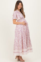 woman wearing a short sleeve floral pink maternity dress, cradling her baby bump while smiling