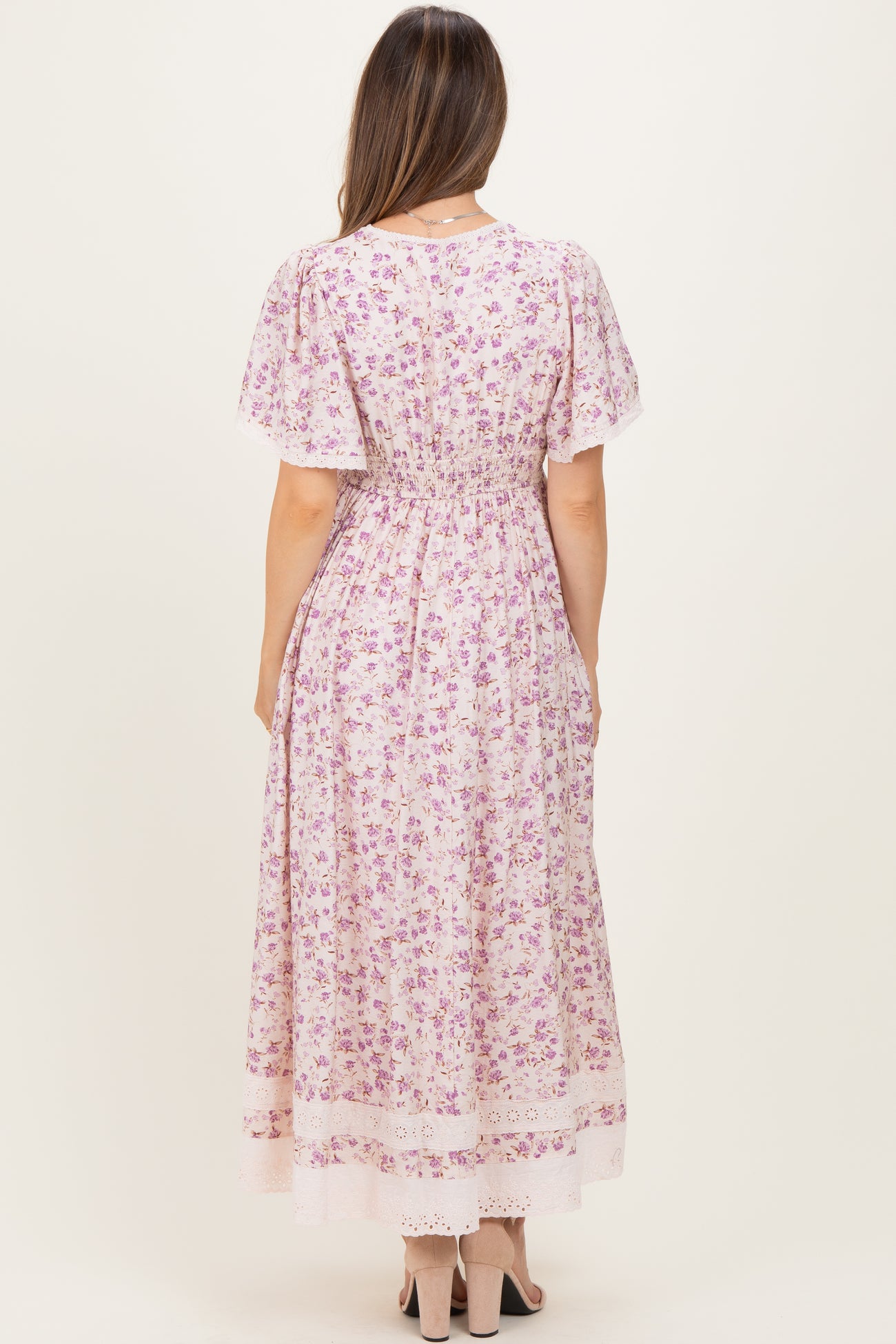woman wearing a floral print pink maternity dress with short sleeves and a fitted waist, showing a baby bump from the back