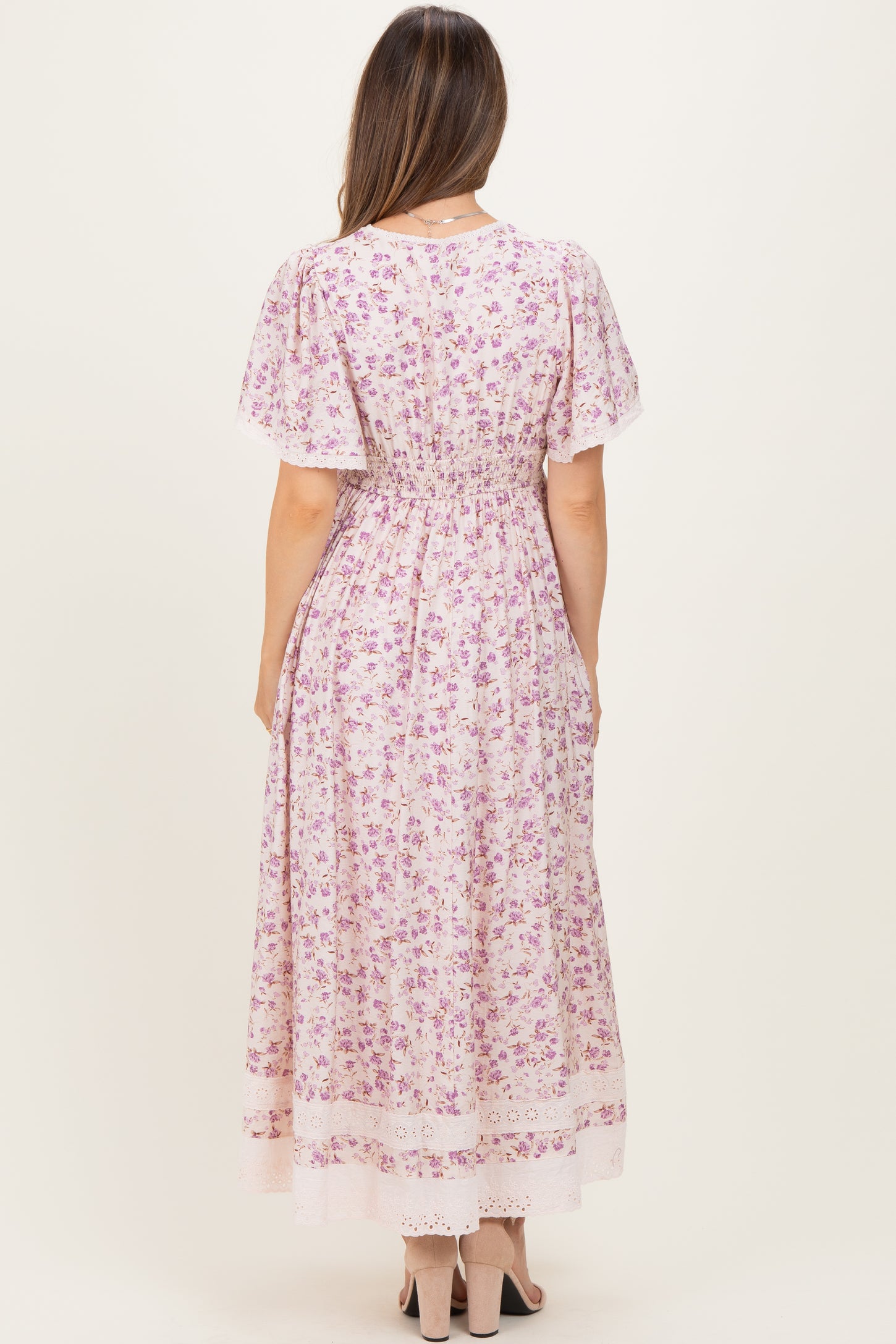 woman wearing a floral print pink maternity dress with short sleeves and a fitted waist, showing a baby bump from the back