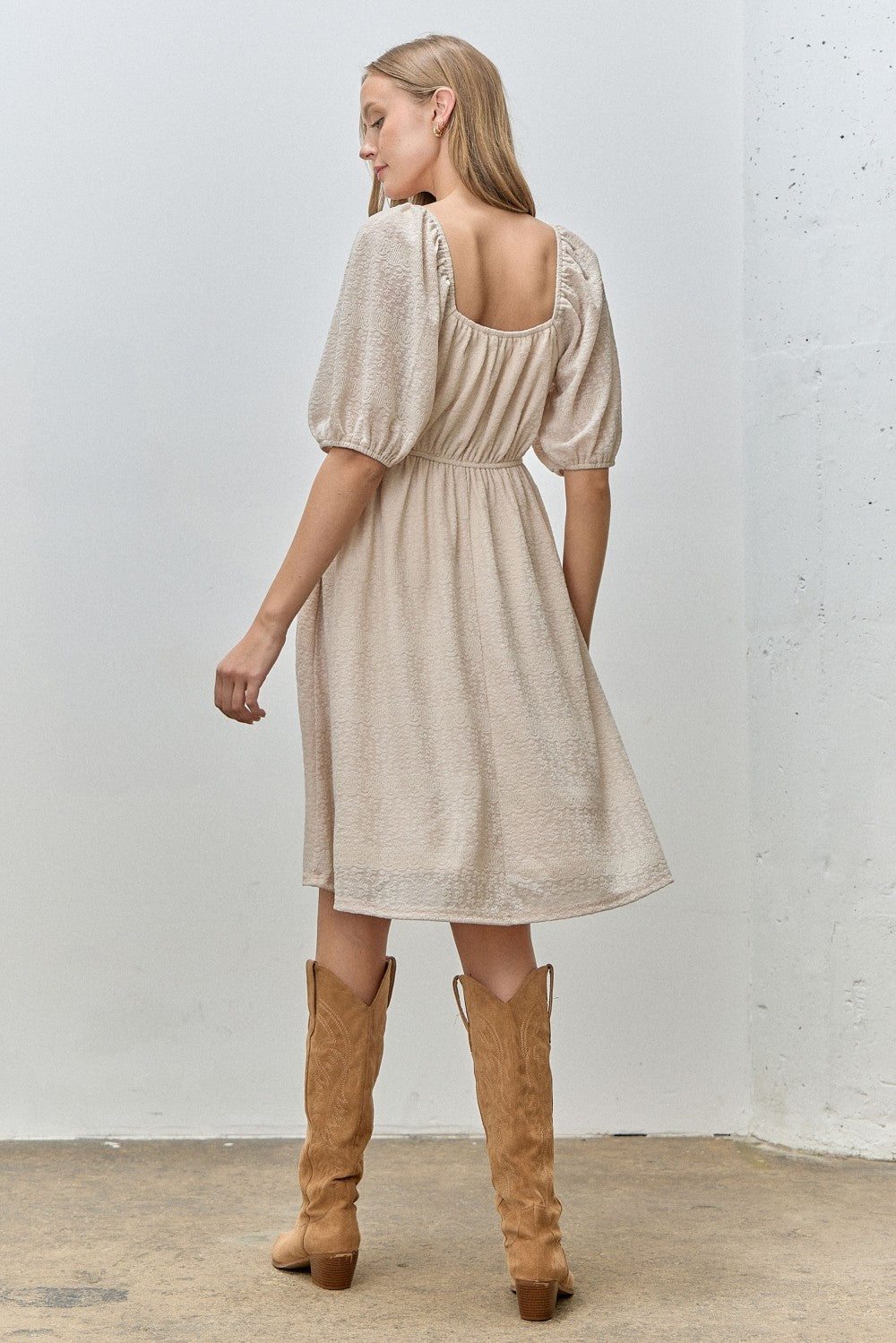 woman wearing a beige short sleeve dress with a square back and puffed sleeves, standing with her back towards the camera