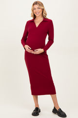 woman wearing a wine red long sleeve maternity dress with a collar and holding her baby bump