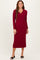 woman wearing a burgundy long sleeve midi dress with a collar and fitted silhouette, standing with a smile