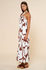 woman wearing a white maxi dress with brown abstract prints and a halter neck style, standing sideways