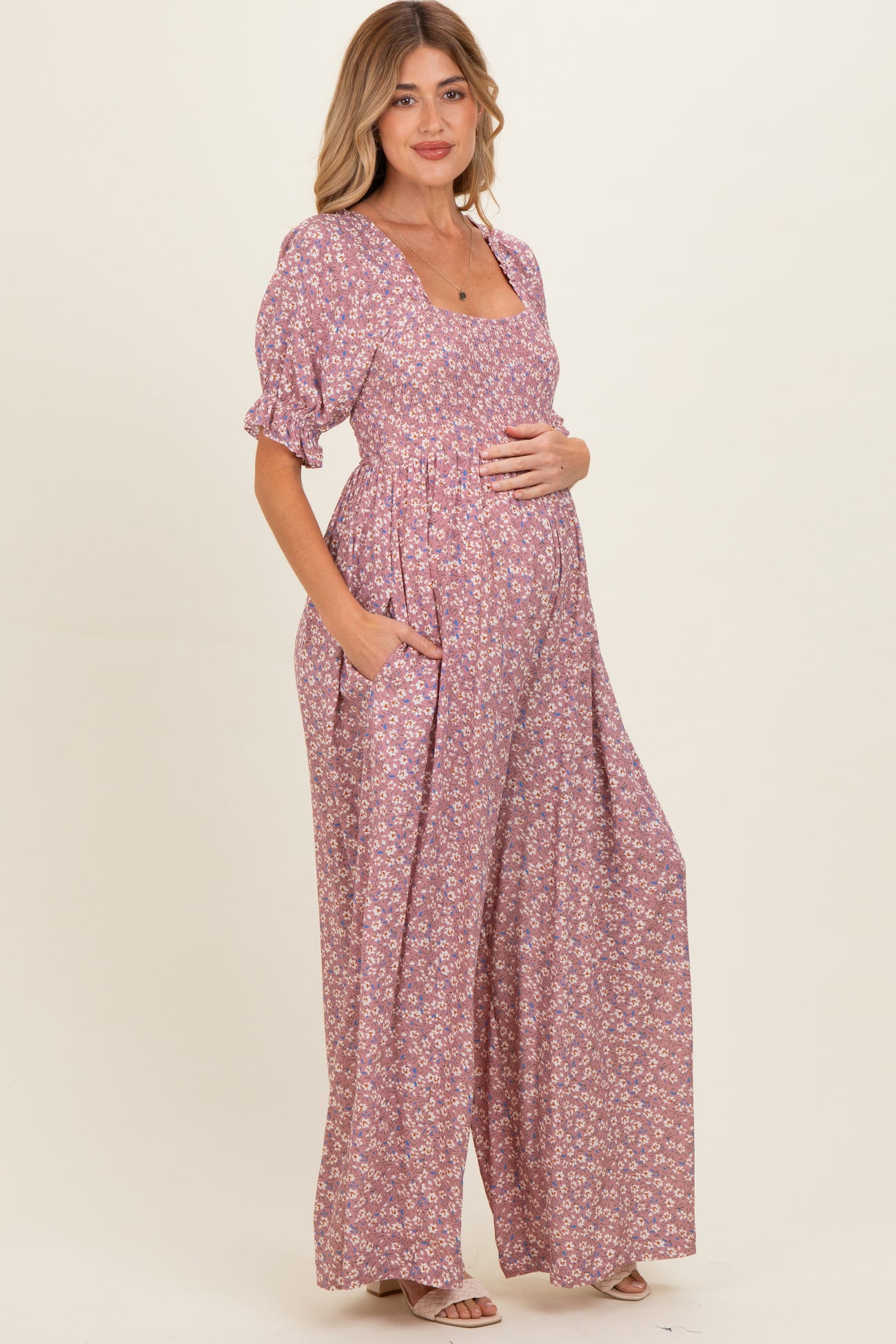 woman wearing a pink floral maternity maxi dress with short puff sleeves and pockets, gently cradling her baby bump
