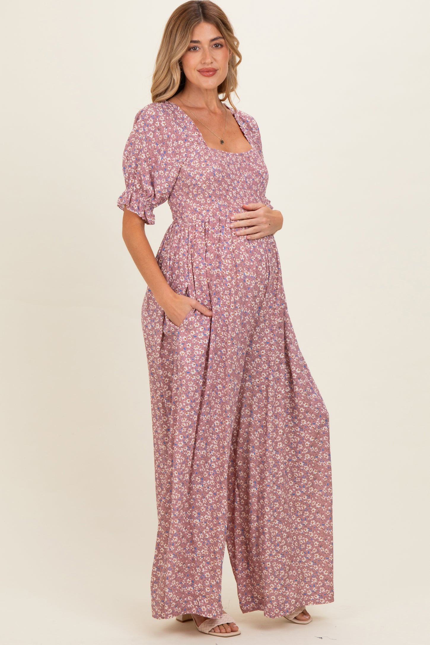 woman wearing a pink floral maternity maxi dress with short puff sleeves and pockets, gently cradling her baby bump