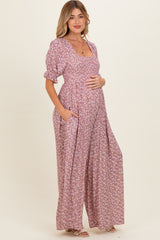 woman wearing a pink floral maternity maxi dress with short puff sleeves and pockets, gently cradling her baby bump